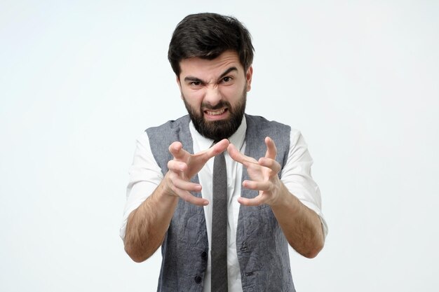 Uomo arrabbiato con barba e capelli scuri che tira le mani verso la telecamera per soffocare qualcuno