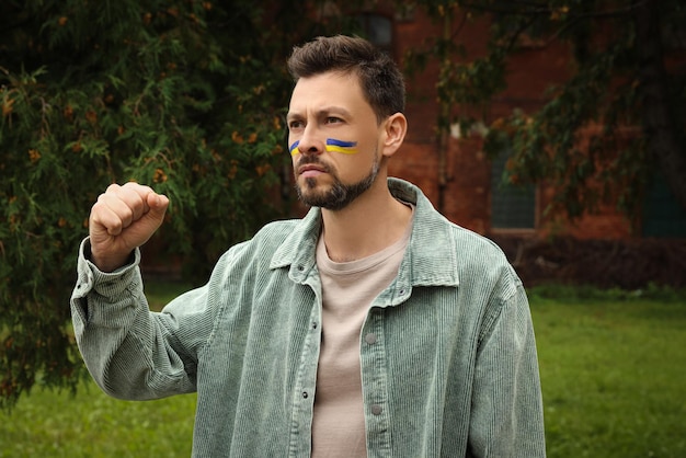 Angry man with drawings of Ukrainian flag on face outdoors