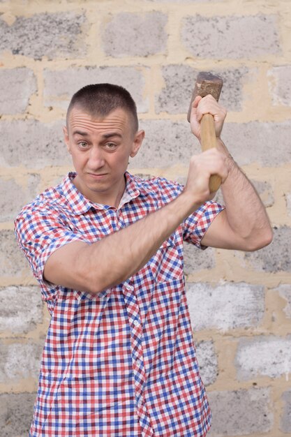 Angry man with sledgehammer on the brick wall