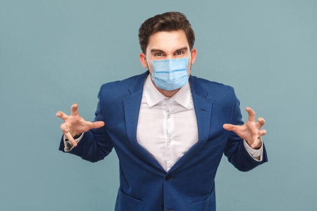 Uomo arrabbiato con maschera medica chirurgica in abito blu che guarda l'obbiettivo