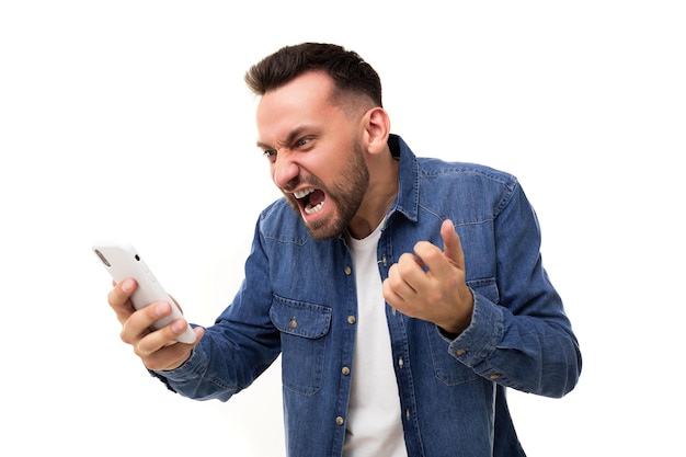 Angry man yells at the phone screen gesturing with his hands with his mouth open and frowning with