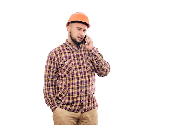 Un lavoratore arrabbiato e nervoso con un casco arancione sta parlando ad alta voce al telefono, gridando al telefono. sfondo bianco isolato