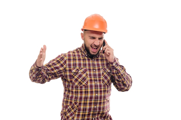 An angry and nervous worker in an orange helmet is talking loudly on the phone, shouting into the phone. Isolated white background