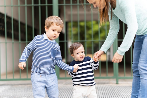 Angry oneyearold baby not wanting to try to walk together with his threeyearold brother and his mother tantrum concept