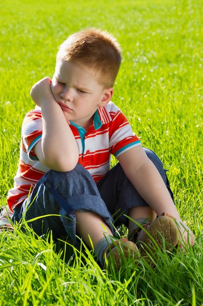 Angry sad boy sitting on grass