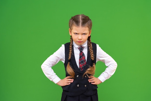 Angry schoolgirl keeps her hands on her sides. isolated green background, copy space.