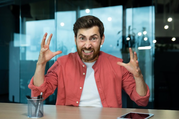 Angry and screaming businessman inside office talking on video call boss in red shirt shouting in