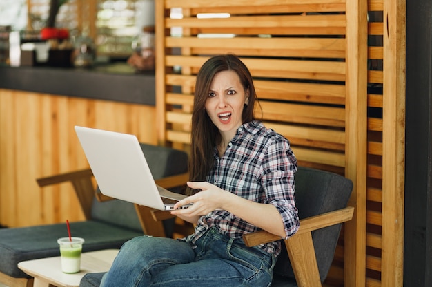 Angry screaming sad upset girl in outdoors street coffee shop wooden cafe sitting with modern laptop pc computer, disturb problem during free time. Mobile Office