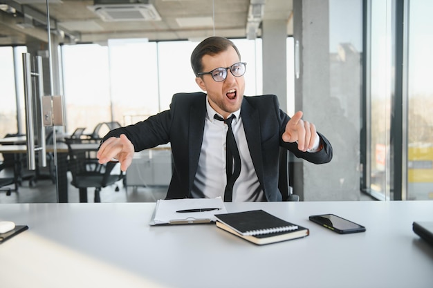 Angry senior businessman sitting at his desk and screaming