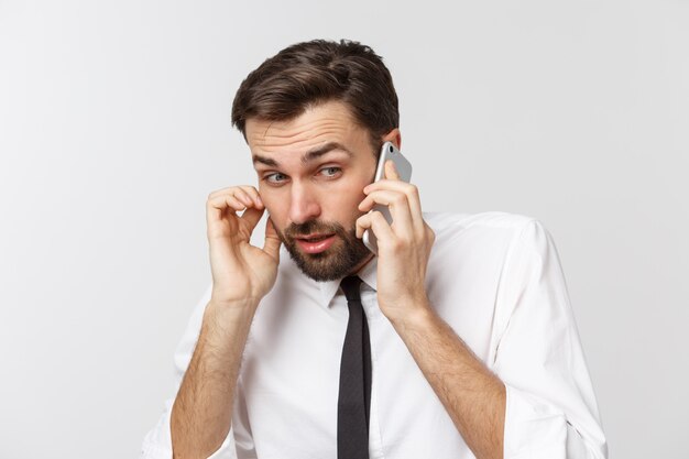 Angry and serious businessman talking on the phone over gray background