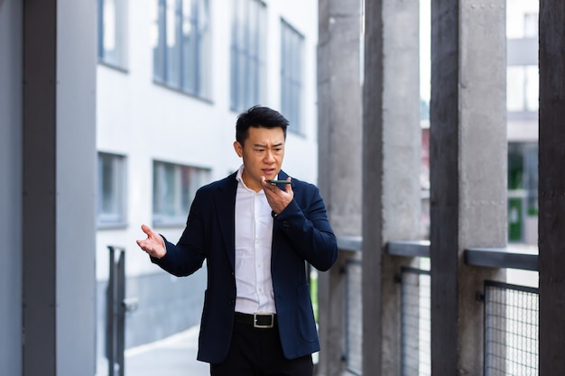 Angry and serious Successful Asian businessman explains information to employees using phone, speaks near office outside