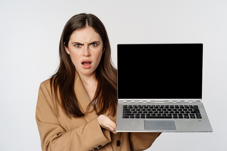 Angry and shocked saleswoman showing laptop screen frowning and staring offended standing over white...