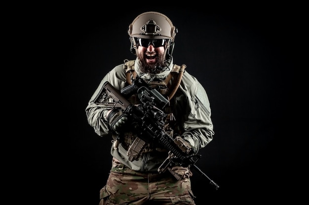 Angry soldier in uniform with a rifle screaming at night commando in stress on a dark background