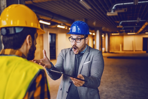 Angry supervisor yelling at his worker because he made mistake on construction. Building in construction process interior.