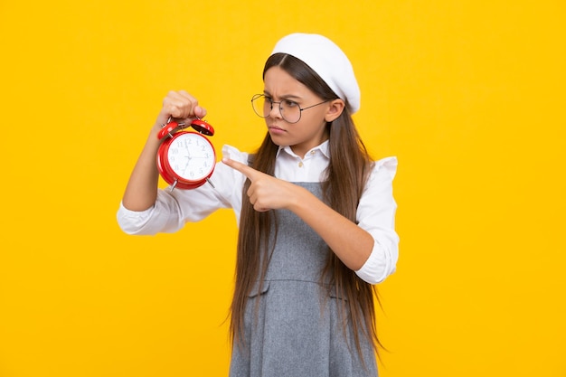 Angry teenager girl upset and unhappy negative emotion of teen student girl with clock isolated on yellow background Child back to school Education and time concept