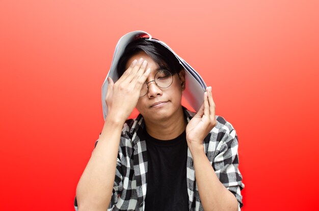 angry and tired of asian male student or worker holding paper work isolated over red background.