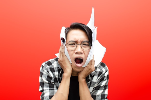 Angry and tired of asian male student or worker holding paper
work isolated over red background.