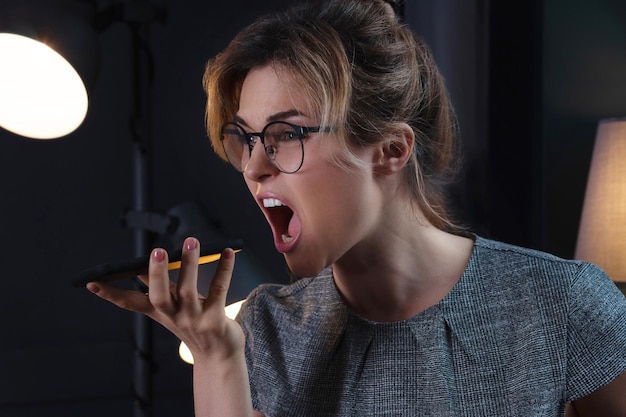 Angry and tired businesswoman yelling into smartphone after long working day