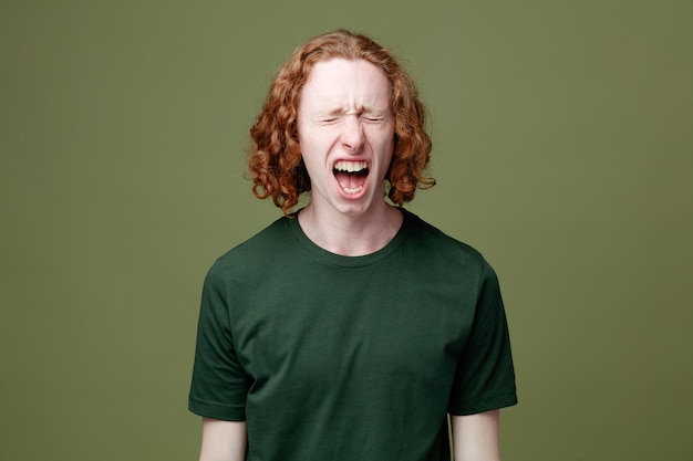 Angry with closed eyes young handsome guy wearing green t shirt isolated on green background