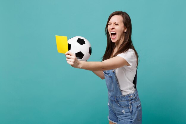 Angry woman football fan support team with soccer ball, yellow\
card, propose player retire from field, swearing isolated on blue\
turquoise background. people emotions, sport family leisure\
concept.