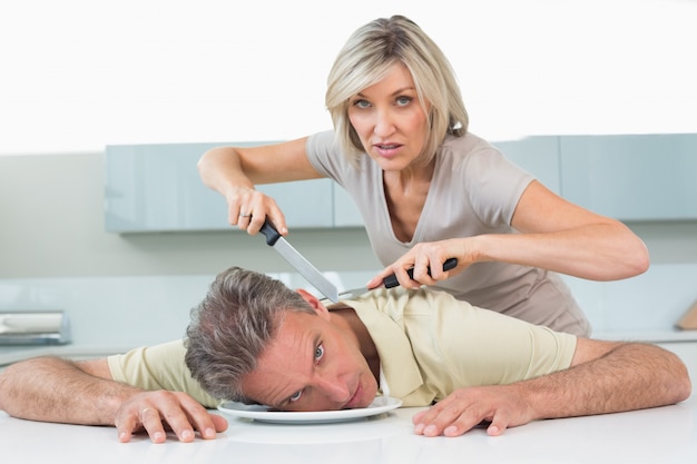 Angry woman holding knife to mans neck in kitchen