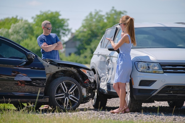 Angry woman and man drivers of heavily damaged vehicles arguing who is guilty in car crash accident on street side Road safety and insurance concept