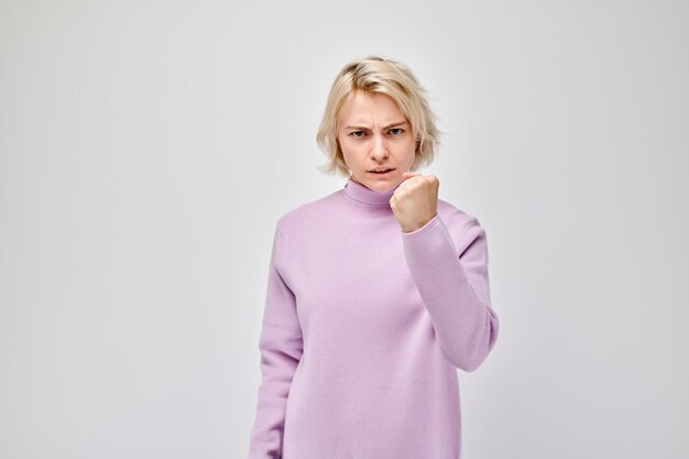 紫色のセーターを着た怒った女性が白い背景に孤立した拳を握っています
