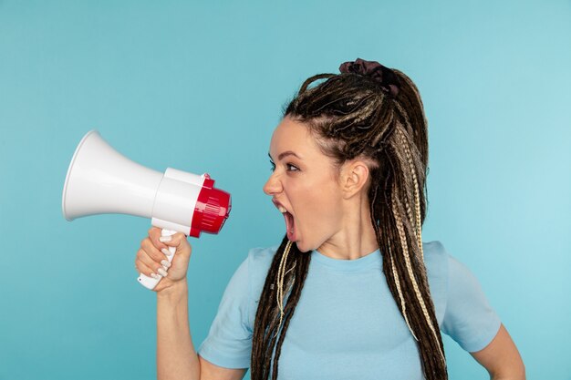 Angry woman screaming to the loudspeaker isolated over the blue wall.