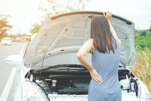 怒っている女性が助けを求めて壊れた車の前に立つ