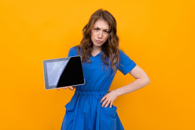 Angry woman with tablet on yellow wall surface, tablet screen with place for text