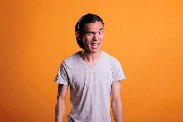 Angry young asian man with furious facial expression, showing\
negative emotions. irritated person screaming, aggressive teenager\
looking at camera, front view studio medium shot