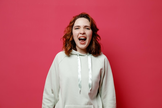 Angry young beautiful girl in white sweater isolated on pink background