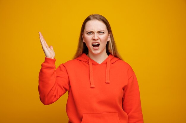 Angry young blonde woman keeping hand in air 