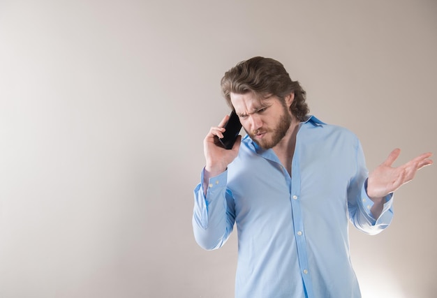 Разгневанный молодой бизнесмен разговаривает по телефону, изолированный на светло-сером фоне.