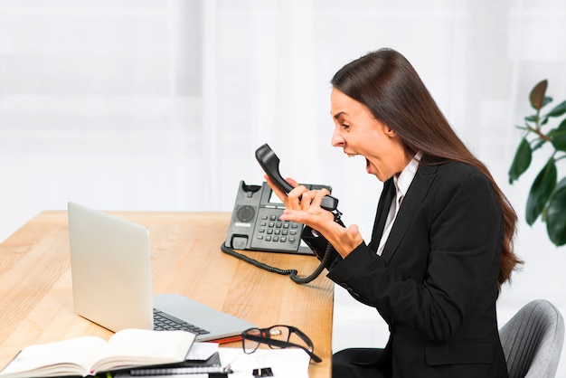 Una giovane donna di affari arrabbiata che si siede sulla sedia che grida sul telefono