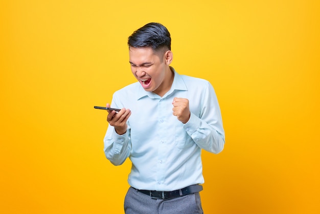 Angry young handsome businessman shouting threatening in loudspeaker on smartphone