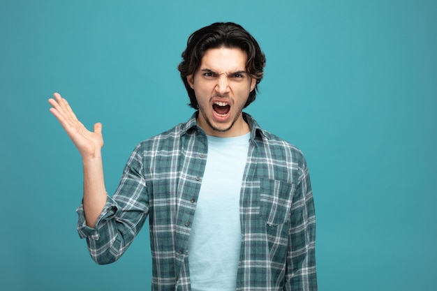 angry young handsome man looking at camera showing empty hand shouting isolated on blue background