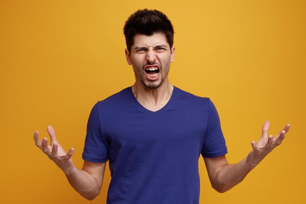 Angry young handsome man looking at camera showing empty hands on yellow background