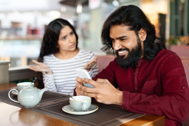 Photo angry young indian woman looking at boyfriend stuck in smartphone