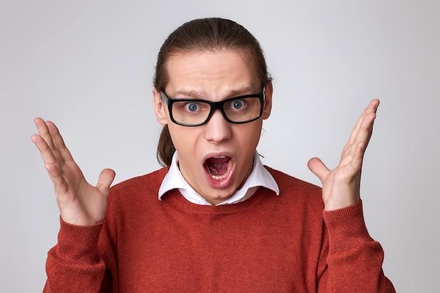 Angry young man in glasses and shirt screaming or shouting isolated on gray background