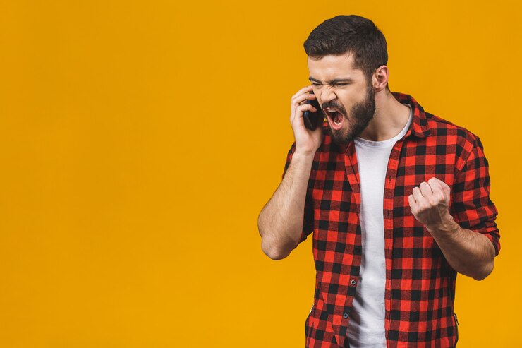 Photo angry young man screaming on the cell phone isolated on a yellow wall.