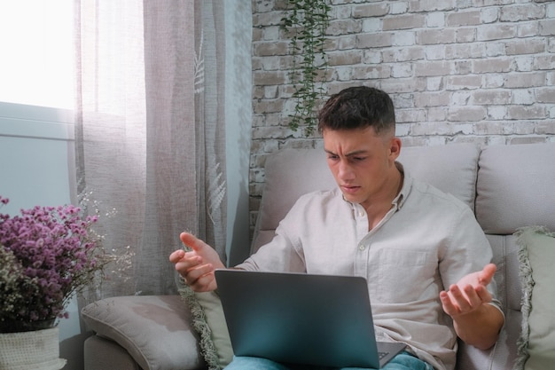 自宅でコンピューター pc を使用して怒っている若い男はソファに座って技術に問題があります