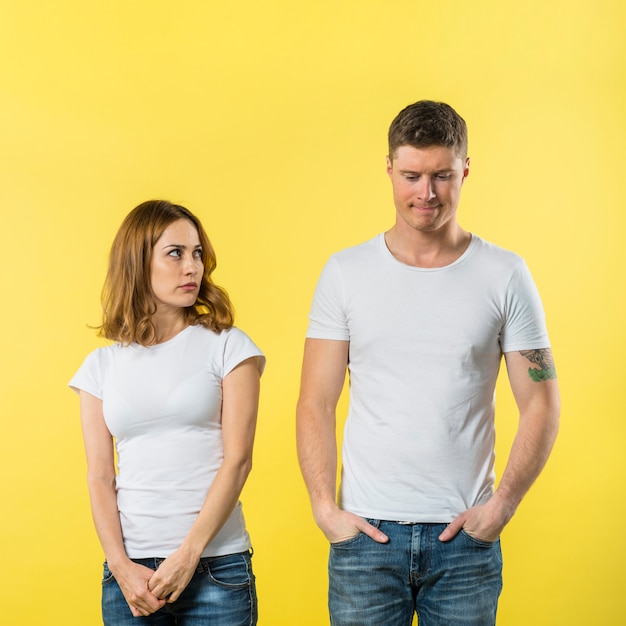 An angry young woman looking at her sad boyfriend against yellow backdrop