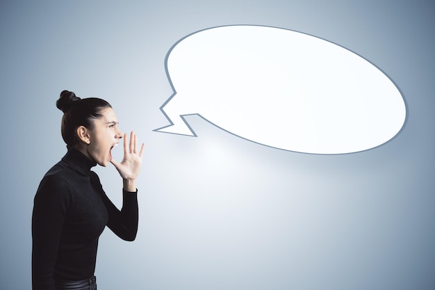 Angry young woman shouting at empty speech bubble on gray background Opinion and mock up place