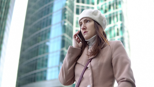 Angry young woman talking on the phone among tall buildings.