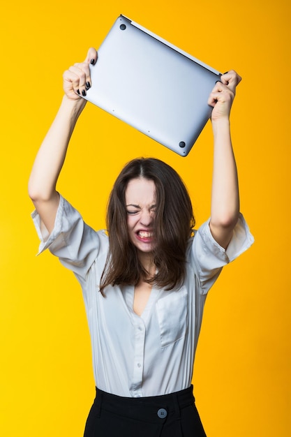 An angry young woman wants to smash a laptop on a yellow background