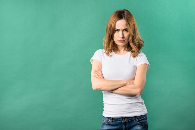 An angry young woman with arms crossed against green backdrop