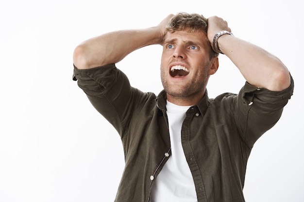 Foto angstige knappe blonde man die handen op het hoofd houdt in paniek schreeuwend bezorgd opkijkend, gek van verontrust en bang poseren bang en bezorgd over grijze muur