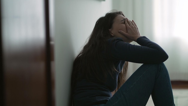 Angstige vrouw zittend op de vloer die thuis aan een psychische aandoening lijdt Eenzame persoon die wanhoop voelt