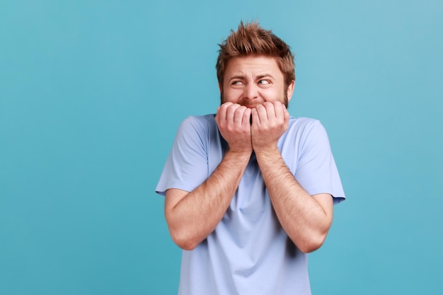 Angststoornis Portret van gestrest bezorgd bebaarde man nagels bijten nerveus over problemen in paniek en op zoek bang Indoor studio shot geïsoleerd op blauwe achtergrond